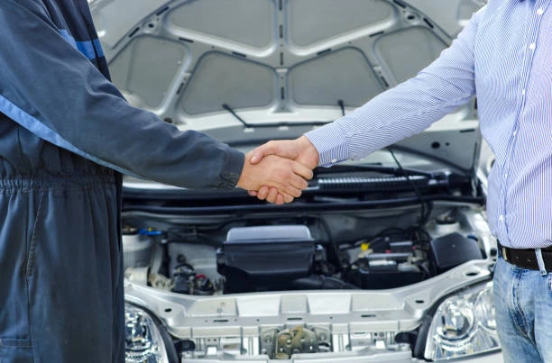 Two people shaking hands beside a car with its bonnet open